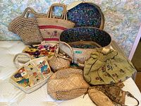 Overview of woven and decorative bags, showing variety of sizes and types in lot on mattress with floral wallpaper background.