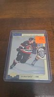 Photo of a Daniel Alfredsson rookie hockey card inside a plastic protective sleeve on a wooden surface.