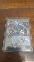 Photo of a Miikka Kiprusoff 2002-03 Signature Series hockey card with autograph in a clear plastic protective case on a wooden surface.