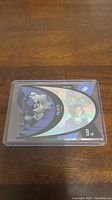 Photo of a Paul Kariya hockey trading card in a protective plastic case on wooden surface. Card has holographic blue and black design with a Toronto Maple Leafs logo and player image.