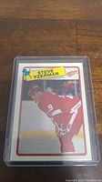 Close-up of Steve Yzerman hockey card in clear plastic protective case on wooden surface.