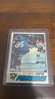 Photo of Syl Apps Pittsburgh Penguins hockey card in protective plastic sleeve, showing front of card with player action image and team logo