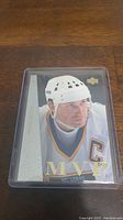 Front view of Wayne Gretzky MVP hockey card in clear protective casing on wood surface.