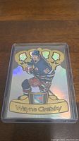 Holographic Wayne Gretzky hockey trading card in blue New York Rangers uniform, with trophies in background and player's name at bottom.