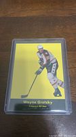 Front image of Wayne Gretzky hockey card showing player in action pose on yellow background, encased in clear plastic protector.