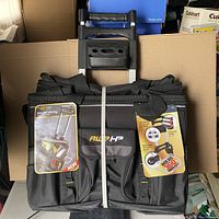 Front view of folded black AWP HP tool bag with telescopic handle folded down and rubber strap securing the bag closed