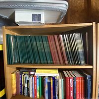 Wide shot showing three shelves of books. Top two shelves contain multiple volumes of MHQ The Quarterly Journal of Military History in green, red, and black covers. Bottom shelf has varied smaller books in mixed colors.