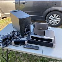 Photo of the Bose stereo system components on a table including speakers, subwoofer, main control unit, remote, and power adapter cables.