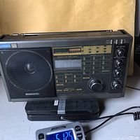 Frontal view of the Magnavox All Weather Radio showing speaker, tuning knobs, and digital display alongside an Accutek digital time device and coiled power cord.