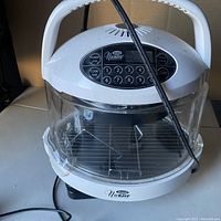 Front view of Mini NuWave oven showing digital control keypad and clear cooking chamber with inside rack, power cord visible.