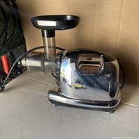 Side angle showing stainless steel body, feeding chute attachment, power cord, and rubber feet.