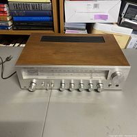 Left angled front view of Realistic STA-64 AM/FM stereo receiver showing wood cabinet side, tuning scale, control knobs and switches, and power cord.