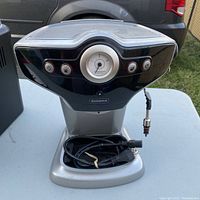 Front view of Starbucks Sirena espresso coffee maker showing control panel with dial and buttons, base with coiled power cord, and steam wand on right side.