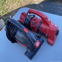 Two handheld Dirt Devil vacuums, one red with cloth dust bag and one black and red with power cord wrapped, displayed on a table outdoors.