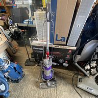 Dyson DC24 upright vacuum cleaner standing upright with cord wrapped on the back, showing front view with dust container visible.