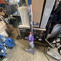 Full view of the Dyson DC50 vacuum cleaner standing upright on a concrete floor, surrounded by other household items.