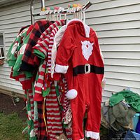 Hanging infant Christmas-themed pajamas on a rack, shows various designs including Santa suit, striped and plaid pajamas