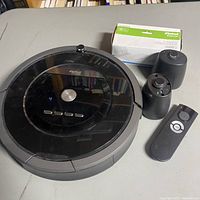 Photo of iRobot Roomba robotic vacuum with remote control, two charging stations, and box of dry sweeping pads.