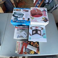 Overview photo of boxed GT Xpress grill, George Foreman grill, Spatula Smart hand mixer, Pedrini biscuit press, and Wilton cake pan set on a table.