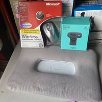 Photo showing Microsoft Wireless IntelliMouse Explorer in original packaging, Logitech C270 HD Webcam box and laptop lap stand.