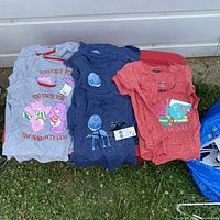 Full overview of 15 children's t-shirts arranged on red container outdoors, showing Care Bears, Star Wars, and Trolls Christmas-themed designs