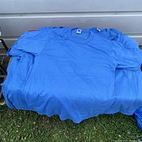 Lot of 22 blue Russell Athletic vintage T-shirts piled on a surface outdoors showing front view and tags