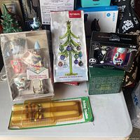 Lot overview showing boxed Nightmare Before Christmas salt and pepper shakers, Thomas Kinkade ornament box, Pier 1 Imports glass Christmas tree box, electric candle lamp with boxed rotating lampshades, and Garfield holiday candles.