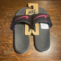 Top view of new Nike Kawa slide sandals in black with pink swoosh, on original cardboard holder.