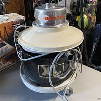 Front angled view showing Oreck label on metal top, black cylindrical body, power cord wrapped around unit and white base with wheels.