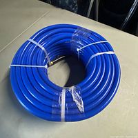 Blue coil pressure washer hose laid on a table, showing coiled construction and plastic ties securing it.