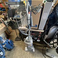 Shark upright vacuum cleaner with hose accessory and power cord wrapped around handle, standing upright among other household items.