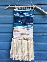 Front view of handwoven wall hanging mounted on driftwood against blue wall.
