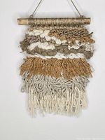 Front view of handwoven wall hanging, showing multiple textured layers in neutral tones with hanging rod