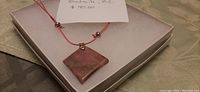 Photo of square rhodonite pendant on pink cord necklace laid on display box showing the overall look.
