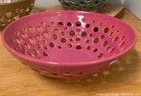 Photo of a pink oval-shaped pottery bowl with multiple round perforations, showcasing the bowl's shape and color.