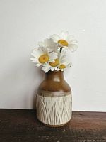 Photo shows a pottery vase with a two-tone finish, brown on top and cream with an engraved pattern on base. The vase contains artificial white daisies with yellow centers.