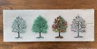 Photo of four seaglass art trees mounted on a whitewashed rectangular wooden panel, arranged side by side in a row.
