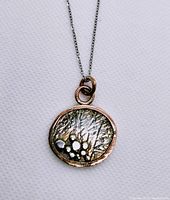 Close-up of the pendant showing the mixed metals and detailed textured design.