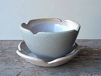 Photo showing side view of handmade ceramic bowl resting in matching scalloped plate, highlighting glaze and shape details.