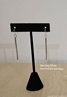 Photo shows the pair of hammered sterling silver earrings displayed on a black earring stand on a wooden surface.