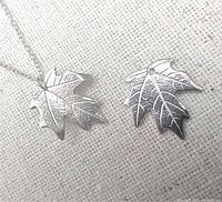 Close-up of sterling silver maple leaf print necklace pendant with chain and matching earrings on beige fabric background.