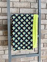 Black cotton blanket side printed with repeated images of Grogu's head with 'May the Force be with you' text on black background, showing green minky dimple backing.