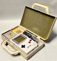 Open carrying case showing console in right compartment, two cartridges in left, power cable coiled at top