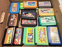 Photo showing 20 assorted vintage Japanese Famicom game cartridges inside a cardboard box. Various colors and artwork visible.