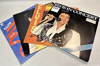 Four Elvis Presley record albums stacked; visible titles include 'Elvis in Concert' and others with colorful covers featuring Elvis Presley.