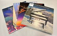 Four Supertramp vinyl record albums stacked and fanned showing colorful front covers including one with a snow-covered grand piano in a mountain setting.