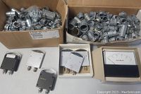 Box of assorted metal plumbing parts including fittings and connectors, behind several analog panel meters.