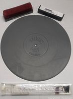 Top-down view showing the gray circular Music Mat turntable mat and both dust pads, one red velvet and one white Odessy dust pad.