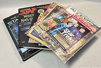 Photo showing a mix of hardcover Star Wars books and several Star Wars-related magazines in plastic sleeves arranged on a gray surface.