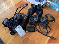 Two pairs of binoculars and a camera on wooden floor, showing overall items in the lot